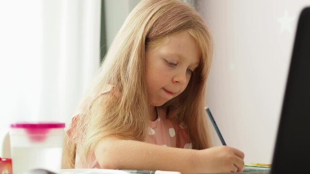 A preschooler girl draws with a pencil and closely follows the teacher online. Online drawing school. A beautiful child is learning to draw. home education