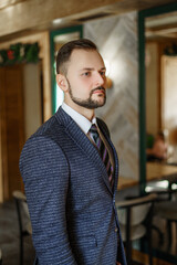 A young man in a business suit looks away. A businessman in a shirt and tie and a dark jacket. A bearded man in a cafe or restaurant.