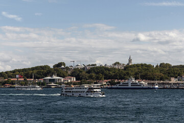 Fototapeta na wymiar View of Bosphorus tour boats passing in front of Topkapi Palace in Istanbul. It is a sunny summer day.