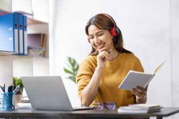 Young adult happy smiling Hispanic Asian student wearing headphones talking on online chat meeting using laptop in university campus or at virtual office. College female student learning remotely.