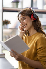 Young adult happy smiling Hispanic Asian student wearing headphones talking on online chat meeting using laptop in university campus or at virtual office. College female student learning remotely.