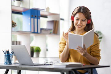 Young adult happy smiling Hispanic Asian student wearing headphones talking on online chat meeting using laptop in university campus or at virtual office. College female student learning remotely.