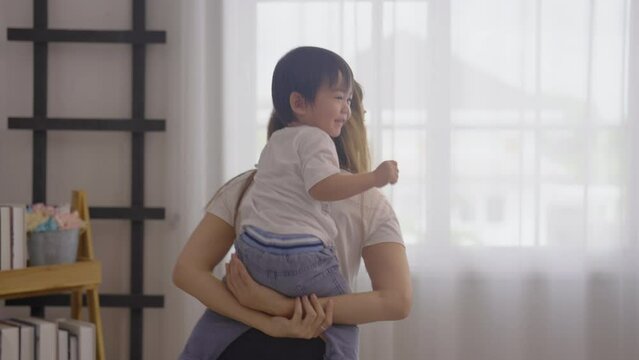 Asian mother hold and play with little son by ride on the back or piggyback in bedroom and they look happy and enjoy together to stay at home.