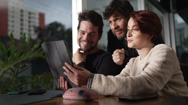 Happy friends discussing content online holding tablet. Three people looking screen together watching video
