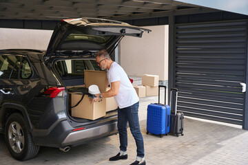 Adult man puts boxes of things in trunk of car.