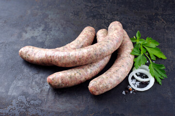 Rohe grobe Allgäuer Bratwurst garniert mit Kräutern und Gewürzen als close-up auf rustikalen schwarzen Hintergrund mit Textfreiraum  © HLPhoto