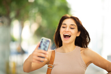 Cheerful young woman taking selfie outside in the city