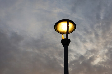 Fototapeta na wymiar Glowing led lamp on background of evening sky with dark clouds. Electric lighting, energy-saving street lantern