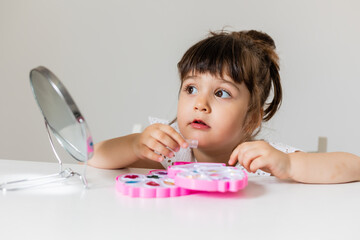 little girl is sitting at the dressing table in front of the mirror and applying makeup. like Mom