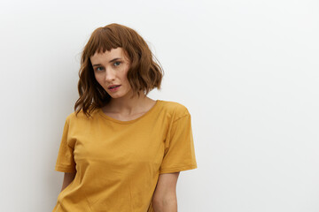 Fototapeta premium a sweet, beautiful, romantic woman in a yellow T-shirt poses on a white background, smiling pleasantly looking at the camera. Horizontal photo with an empty space for inserting an advertising layout