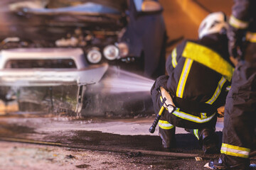 Group of fire men extinguishing and put out burning car crash after road traffic incident, fire fighting operation in the night city, firefighters with fire engine truck vehicle, emergency and rescue