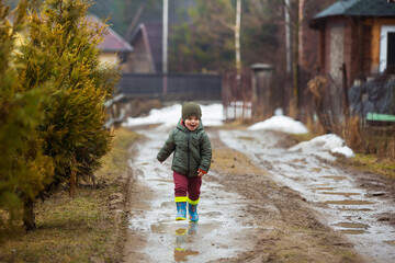 Little boy in protective rubber boots and rain clothes jumping in mud puddle. Happy child having...