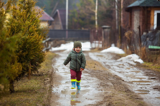 Little boy in protective rubber boots and rain clothes jumping in mud puddle. Happy child having fun while playing in puddle after rain.