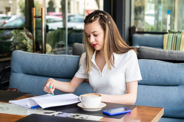 Beautiful young lady holding notebook and looking at it at the restaurant