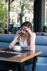Fototapeta premium Tired young lady is talking on the phone and sitting at the restaurant