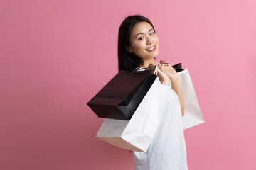Shopping asian happy woman holding shopping bags on pink background.