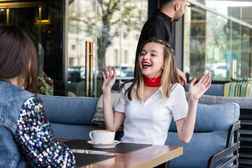 Happy young lady talking with her friend at the restaurant and laughing