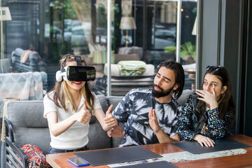 young girl wearing Vr set and sitting with her friends at the cafe