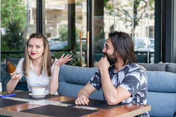 Young girl sitting at the restaurant with her boyfriend and smiling for the camera