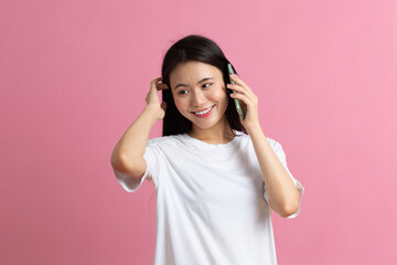 Smiling asian woman speaking mobile phone standing on pink background