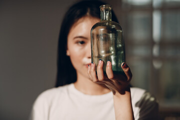 Asian young adult woman hold green glass bottle front face with day sunlight indoor interior