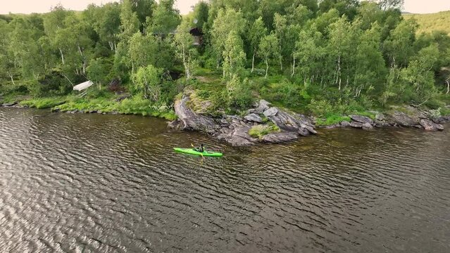 Close up aerial drone video above girl paddling in green kayak, mountain lake in Scandinavian mountains. Norway, Sweden