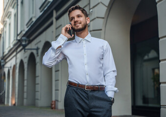 Portrait of businessperson dressed in white shirt talking on cellphone outdoors in city street.