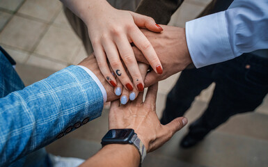 Portrait of business meeting of four people holding their hands together outdoors in city.
