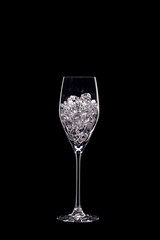 Champagne flute filled with transparent crystals backlit and isolated on black background. Beverage glassware concept. Copy space.
