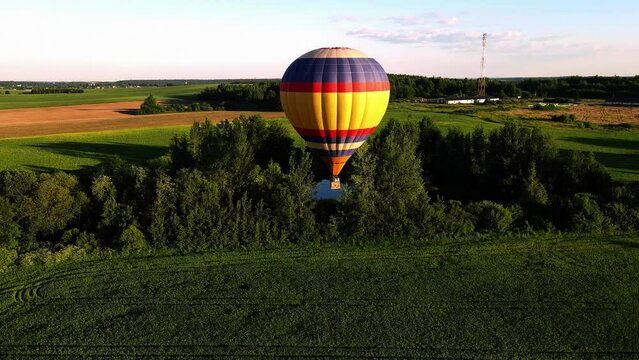 the balloon is flying close to the ground, next to the trees