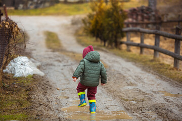 Little boy in protective rubber boots and rain clothes jumping in mud puddle. Happy child having...