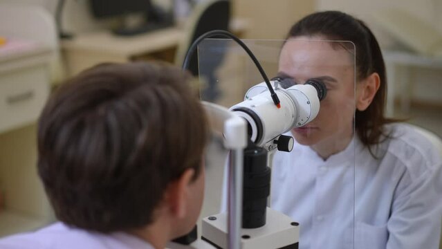 Portrait of professional concentrated woman examining man eye with slit lamp in hospital. Serious focused ophthalmologist doing medical examination of patient in medical clinic. Health care concept