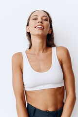 A woman poses on a white wall background in pants and T-shirt and smiles beautifully at home. Healthy and beautiful facial and body skin