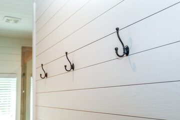 A set of black rustic farmhouse or industrial style hanging hooks on white shiplap planks in a...