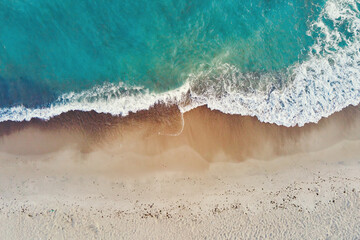 Sand beach with sea waves, top view. Summer vacation and travel concept. Beautiful coastline with blue sea and sand beach, aerial view