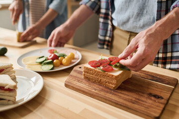 Close-up of young couple cooking sandwiches with vegetables for breakfast together at table