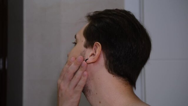 Young man examining his face while watching into t