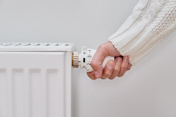 Woman adjusting temperature on heating radiator, Energy crisis concept in Europe, Rising costs in...