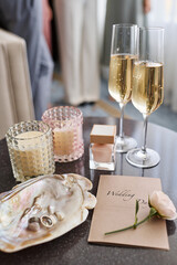 Wedding composition with two cocktails, flutes of champagne, bottle of scent, invitation in envelope, fresh white rose and rings in pearl shell