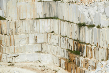 Part of white thick and tall stone wall surrounding territory of large modern production factory situated on marble quarry