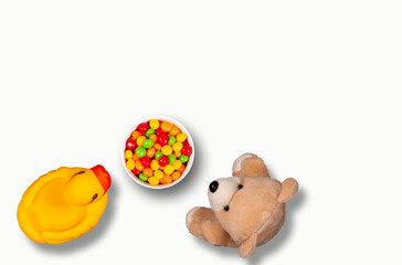 Rubber duck and teddy bear looking at a bowl of colorful candy. Top view