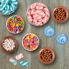 Colorful candies, marshmellows, chocolate balls in jars, lollipops and sweet peanuts on wooden background