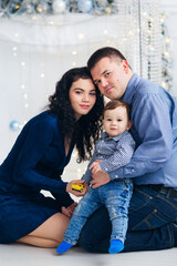 parents and little son sitting on floor near fireplace and looking at camera. Christmas photo session.