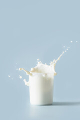 Splash of fresh organic milk in glass on blue background. Vertical format.