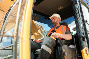 Male builder or driver of construction machine in workwear and hardhat operating caterpillar truck...