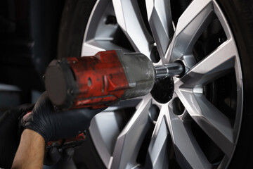 Close up of Mechanic is Unscrewing Lug Nuts with Pneumatic Impact Wrench. Repairman Works in a Modern Car Service. Specialists Removes the Wheel in Order to Fix a Component on a Vehicle