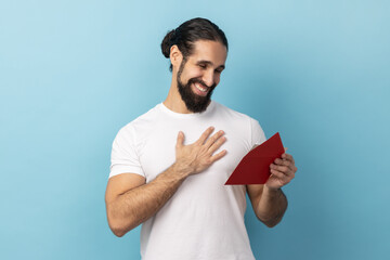 Portrait of man with beard wearing T-shirt reading letter from red envelope, gets greeting card,...