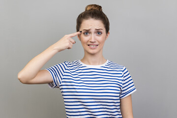 Crazy idea. Portrait of woman wearing striped T-shirt showing stupid gesture, looking with...