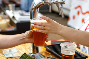 The hand holds a plastic glass with beer.