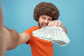 Portrait of crazy rich man with Afro hairstyle wearing orange T-shirt showing many dollars...